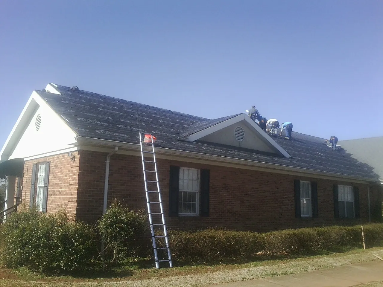 Crew tearing shingles off a brick ranch roof with a ladder set — Emergency Roof Repair work by our crew in Russell
